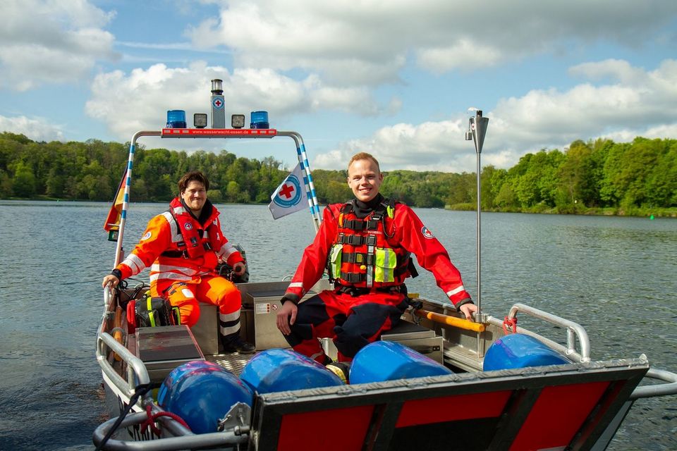 Zwei Mitglieder der Wasserwacht in einem Boot auf einem See, die in die Kamera lächeln